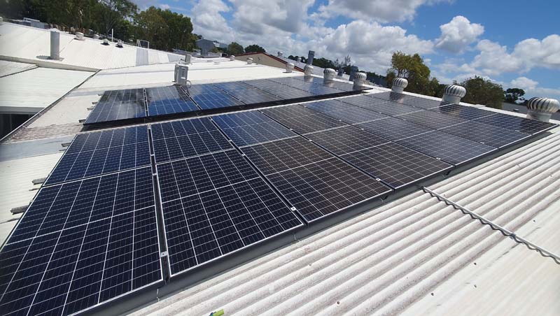Rooftop row of dark blue solar panels on a white metal roof under a partly cloudy sky.
